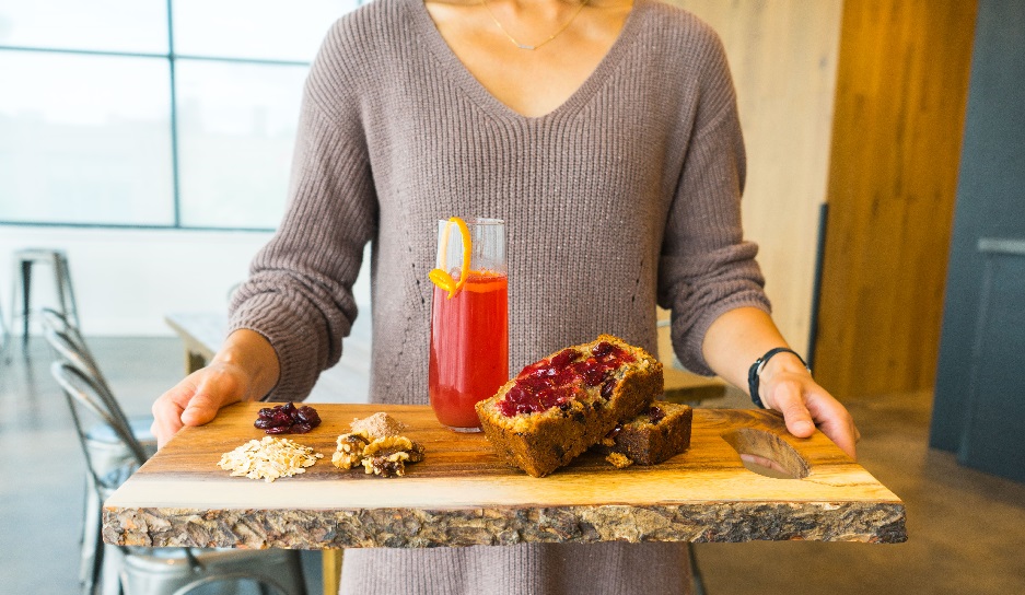 A woman holding a tray with an alcoholic beverage with a slice of Christmas bread.