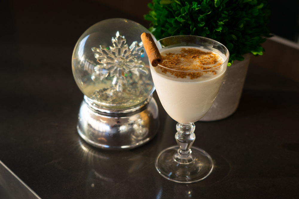 Egg nog served in a Nick and Nora drinking glass with a snowglobe in the background.