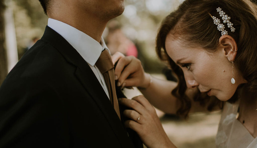 Bride adjusting the boutonnière on the groom's tux lapel.